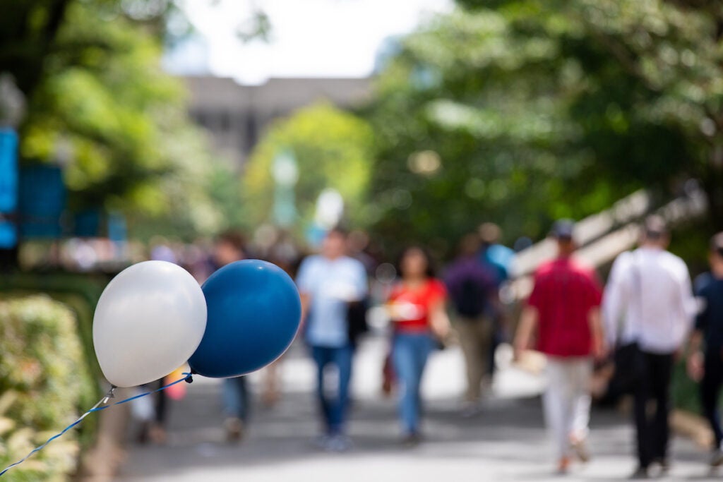 A blue and a white balloon wave in the breeze, students walk through campus in the background during new student orientation